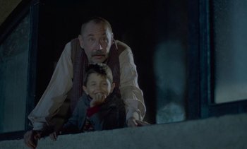 Movie still from “Cinema Paradiso” (1988), directed by Giuseppe Tornatore – An older man and a young boy pose for a picture; Medium shot, Low angle