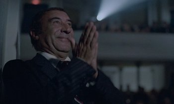 Movie still from “Cinema Paradiso” (1988), directed by Giuseppe Tornatore – A man in a suit claps his hands in front of a projector; Close Up shot, Low angle