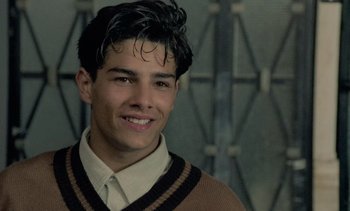 Movie still from “Cinema Paradiso” (1988), directed by Giuseppe Tornatore – A young man smiles for the camera in front of a wall; Close Up shot, Over the shoulder angle
