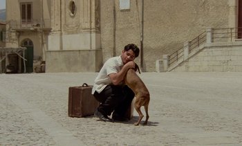 Movie still from “Cinema Paradiso” (1988), directed by Giuseppe Tornatore – A man kneeling down next to a brown dog; Wide shot, Low angle