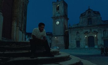 Movie still from “Cinema Paradiso” (1988), directed by Giuseppe Tornatore – A man sitting on steps in front of an old building; Wide shot, Low angle