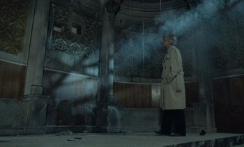 Movie still from “Cinema Paradiso” (1988), directed by Giuseppe Tornatore – An older man in a trench coat standing in front of a pillar with smoke coming out of it; Wide shot, Low angle