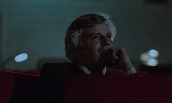 Movie still from “Cinema Paradiso” (1988), directed by Giuseppe Tornatore – A man sitting in a chair with a cell phone to his ear; Close Up shot, Low angle