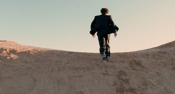 Movie still from “The Tree of Life” (2011), directed by Terrence Malick – A man in a black suit is walking up a hill; Extreme Wide shot, High angle