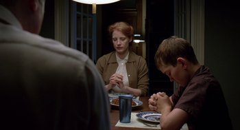 Movie still from “The Tree of Life” (2011), directed by Terrence Malick – A woman sitting at a table with two men praying; Medium shot, Over the shoulder angle