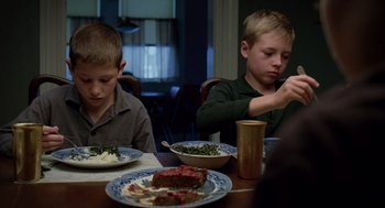 Movie still from “The Tree of Life” (2011), directed by Terrence Malick – Two young boys sitting at a dinner table eating food; Medium shot, Low angle