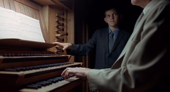 Movie still from “The Tree of Life” (2011), directed by Terrence Malick – A man in a suit and tie playing an organ; Medium shot, Low angle