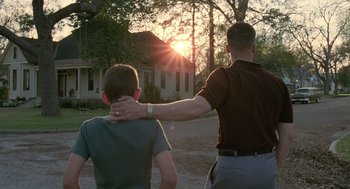 Movie still from “The Tree of Life” (2011), directed by Terrence Malick – A man and a boy are standing arm in arm in front of a house; Medium shot, Low angle