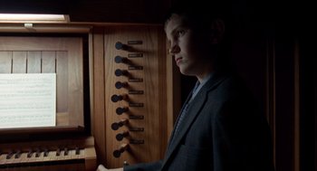 Movie still from “The Tree of Life” (2011), directed by Terrence Malick – A man in a suit standing in front of a wooden cabinet; Medium shot, Low angle