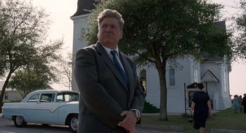 Movie still from “The Tree of Life” (2011), directed by Terrence Malick – A man standing in front of a building with his arms crossed; Medium shot, Low angle