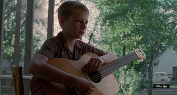 Movie still from “The Tree of Life” (2011), directed by Terrence Malick – A young boy is playing an acoustic guitar outside; Close Up shot, Low angle