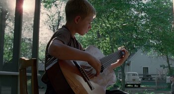 Movie still from “The Tree of Life” (2011), directed by Terrence Malick – A young boy is playing an acoustic guitar; Medium shot, Low angle