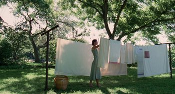 Movie still from “The Tree of Life” (2011), directed by Terrence Malick – A woman hanging clothes on a clothesline in a yard; Wide shot, Low angle