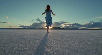 A woman in a blue dress is running across a field