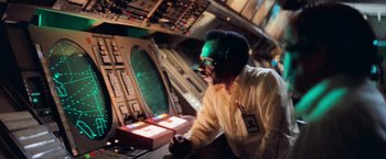 Movie still from “Close Encounters of the Third Kind” (1977), directed by Steven Spielberg – A man with a face mask on looking at a computer screen; Medium shot, Low angle