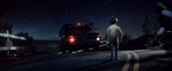 Movie still from “Close Encounters of the Third Kind” (1977), directed by Steven Spielberg – A boy standing on the side of the road looking at a truck; Wide shot, Low angle