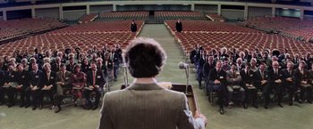 Movie still from “Close Encounters of the Third Kind” (1977), directed by Steven Spielberg – A man standing at a podium in front of a group of people; Extreme Wide shot, High angle