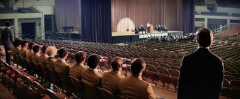 Movie still from “Close Encounters of the Third Kind” (1977), directed by Steven Spielberg – A group of people sitting in chairs in front of an audience; Extreme Wide shot, High angle