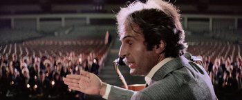 Movie still from “Close Encounters of the Third Kind” (1977), directed by Steven Spielberg – A man in a gray suit is holding a microphone; Close Up shot, Low angle