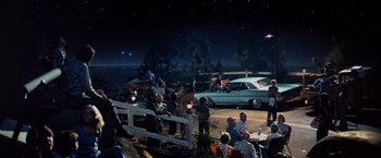 Movie still from “Close Encounters of the Third Kind” (1977), directed by Steven Spielberg – A group of people standing around a car on a street; Extreme Wide shot, High angle