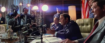 Movie still from “Close Encounters of the Third Kind” (1977), directed by Steven Spielberg – A group of men sitting at a table with microphones; Medium shot, Over the shoulder angle