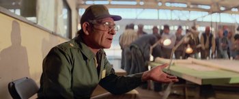 Movie still from “Close Encounters of the Third Kind” (1977), directed by Steven Spielberg – An older man wearing a hat and glasses talking; Medium shot, Over the shoulder angle