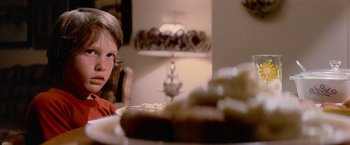 Movie still from “Close Encounters of the Third Kind” (1977), directed by Steven Spielberg – A young boy sitting at a table with a plate of food; Close Up shot, Over the shoulder angle