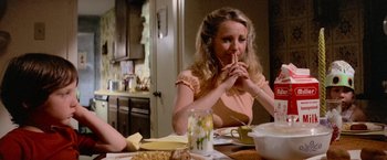 Movie still from “Close Encounters of the Third Kind” (1977), directed by Steven Spielberg – A woman sitting at a table with a plate of food in front of her mouth; Medium shot, Low angle