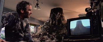 Movie still from “Close Encounters of the Third Kind” (1977), directed by Steven Spielberg – A man is watching television in front of a pile of rubble; Wide shot, Low angle