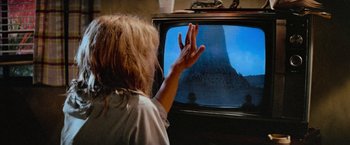 Movie still from “Close Encounters of the Third Kind” (1977), directed by Steven Spielberg – A person with blonde hair is waving at a television screen; Extreme Close Up shot, Over the shoulder angle