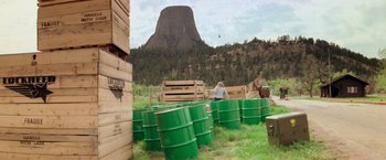 Movie still from “Close Encounters of the Third Kind” (1977), directed by Steven Spielberg – A group of green barrels sitting in the grass near a mountain; Extreme Wide shot, Over the shoulder angle
