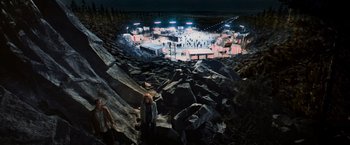 Movie still from “Close Encounters of the Third Kind” (1977), directed by Steven Spielberg – A person standing on a rock formation in front of a stage; Extreme Wide shot, High angle