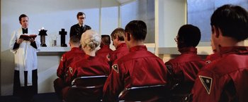 Movie still from “Close Encounters of the Third Kind” (1977), directed by Steven Spielberg – A group of people in red jackets sitting in a room; Medium shot, Over the shoulder angle