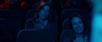 Movie still from “Clouds” (2020), directed by Justin Baldoni – A woman sitting in a movie theater with her hand on her chin; Medium shot, Over the shoulder angle