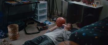 Movie still from “Clouds” (2020), directed by Justin Baldoni – A young man laying on the ground holding a basketball; Wide shot, High angle