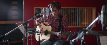 Movie still from “Clouds” (2020), directed by Justin Baldoni – A young man playing an acoustic guitar in a recording studio; Medium shot, Low angle