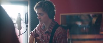 Movie still from “Clouds” (2020), directed by Justin Baldoni – A young man wearing headphones while holding a guitar; Close Up shot, Over the shoulder angle