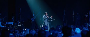 Movie still from “Clouds” (2020), directed by Justin Baldoni – A man standing on a stage holding a microphone; Wide shot, Over the shoulder angle