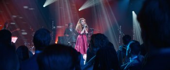 Movie still from “Clouds” (2020), directed by Justin Baldoni – A woman singing into a microphone in front of an audience; Wide shot, Over the shoulder angle