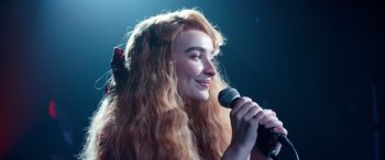 Movie still from “Clouds” (2020), directed by Justin Baldoni – A woman with long red hair is holding a microphone; Close Up shot, Over the shoulder angle