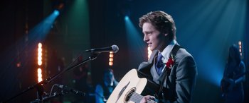 Movie still from “Clouds” (2020), directed by Justin Baldoni – A man in a suit and tie playing an acoustic guitar; Medium shot, Over the shoulder angle