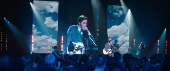 Movie still from “Clouds” (2020), directed by Justin Baldoni – A man in a suit and tie is on a stage with a microphone; Wide shot, Low angle