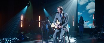 Movie still from “Clouds” (2020), directed by Justin Baldoni – A man in a suit and tie holding a guitar; Wide shot, Over the shoulder angle