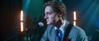 Movie still from “Clouds” (2020), directed by Justin Baldoni – A man in a gray suit and blue tie is speaking into a microphone; Close Up shot, Over the shoulder angle