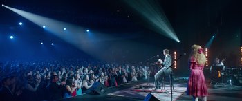 Movie still from “Clouds” (2020), directed by Justin Baldoni – A man in a gray suit is on a stage with a microphone; Extreme Wide shot, Over the shoulder angle