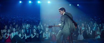 Movie still from “Clouds” (2020), directed by Justin Baldoni – A man in a suit playing a guitar in front of an audience; Wide shot, Over the shoulder angle
