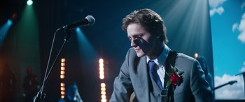 Movie still from “Clouds” (2020), directed by Justin Baldoni – A man in a gray suit and a microphone; Medium shot, Over the shoulder angle