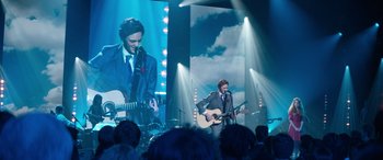Movie still from “Clouds” (2020), directed by Justin Baldoni – A man in a suit and tie playing a guitar and singing; Wide shot, Over the shoulder angle