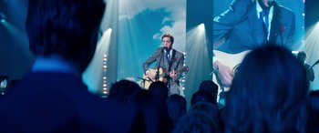 Movie still from “Clouds” (2020), directed by Justin Baldoni – A man in a suit and tie playing a guitar in front of an audience; Wide shot, Over the shoulder angle