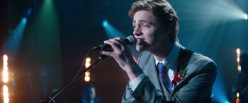 Movie still from “Clouds” (2020), directed by Justin Baldoni – A man in a suit and tie holding a microphone and singing; Medium shot, Over the shoulder angle